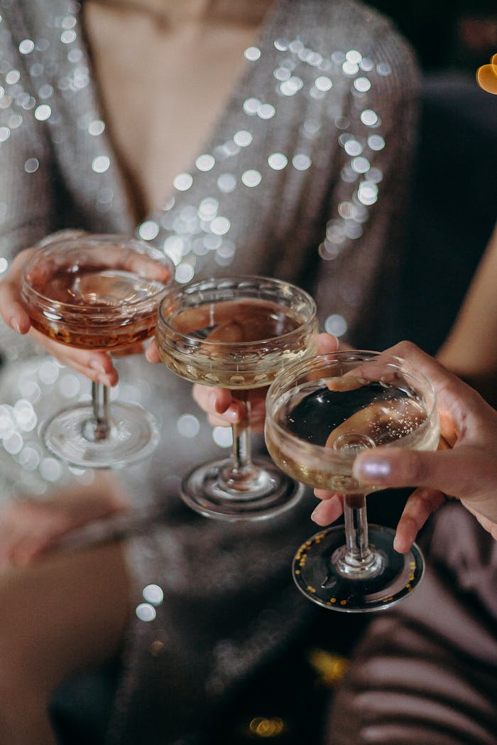 Three people clinking glasses filled with cocktails during a celebration with shimmering attire.